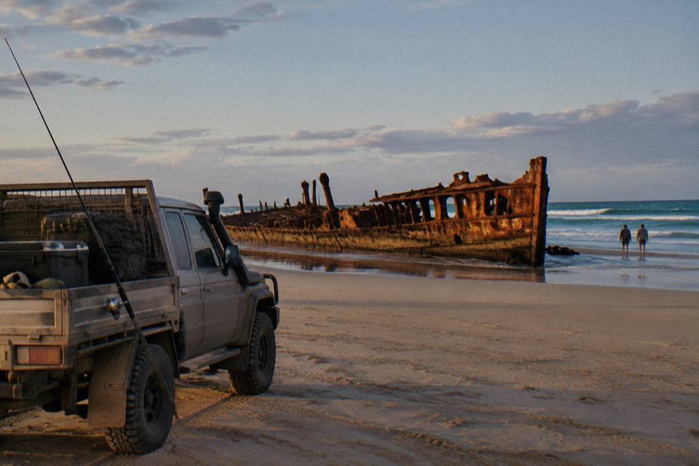 A four wheel drive vehicle parked on a wide sandy beach beside blue ocean