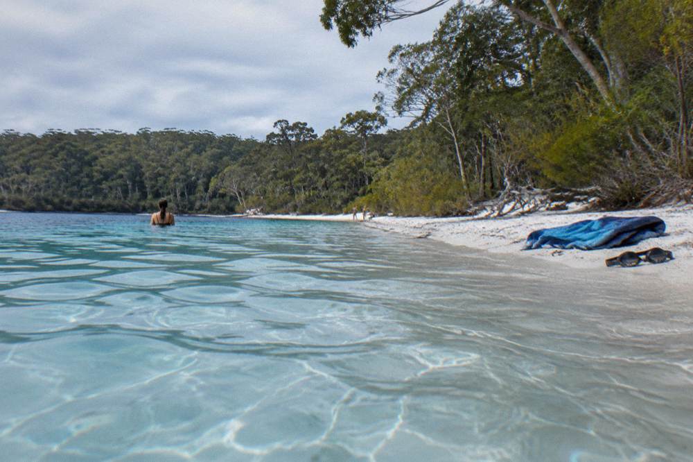 A clear blue freshwater lake with white sand shore and surrounding trees