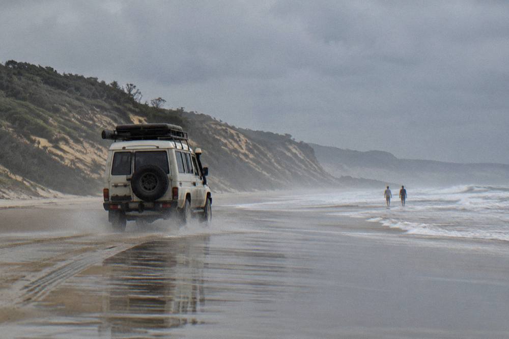 A four wheel drive coach driving along a wide sandy beach with ocean on one side