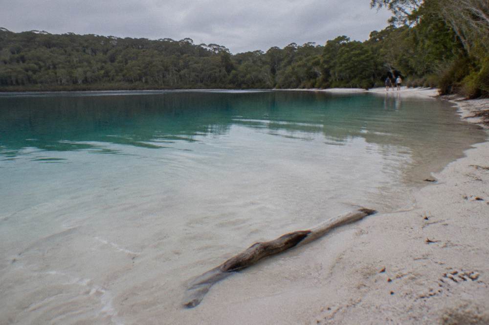 Clear turquoise freshwater lake ringed by pale sand and forest