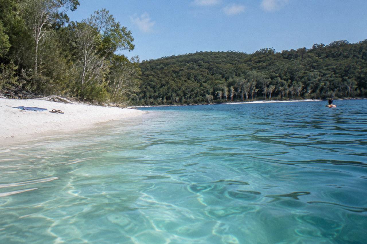 Clear turquoise water of a freshwater lake ringed by white sand and forest