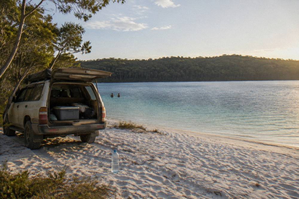 A four wheel drive vehicle parked on pale sand beside a calm freshwater lake