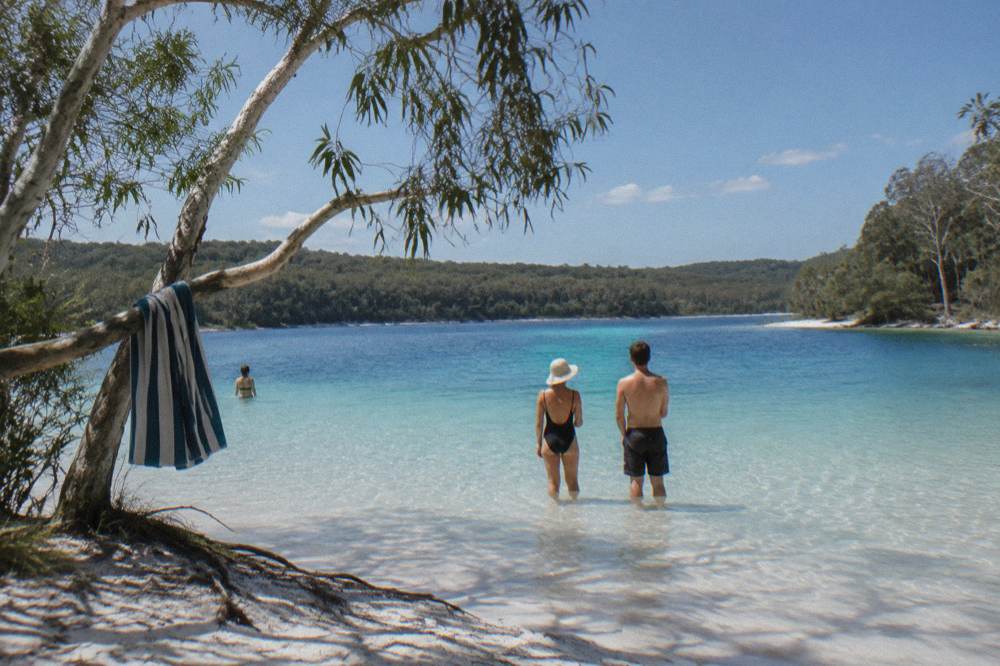 A group of travellers standing on white sand at the edge of a turquoise lake