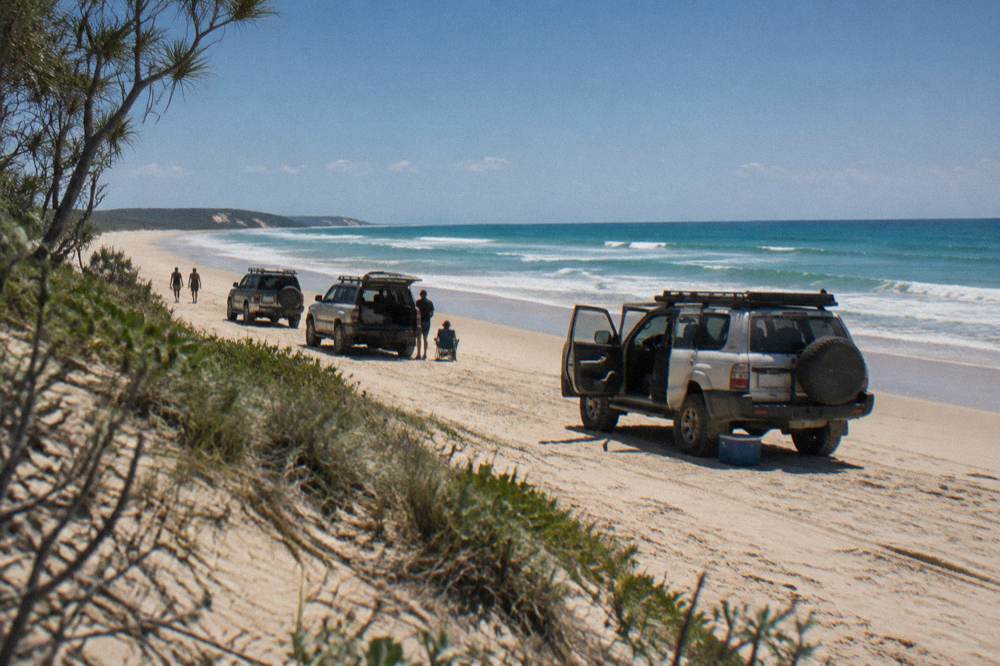 A group of four wheel drive vehicles parked on a wide sand beach beside blue ocean