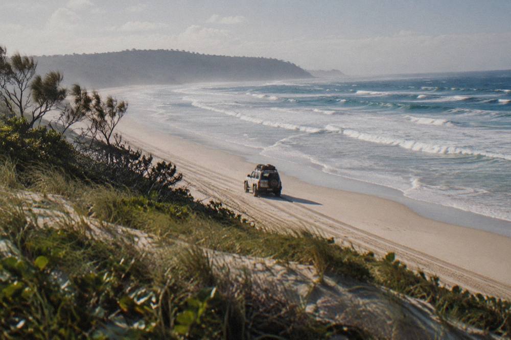 Tour coach driving along a firm sandy beach track with ocean on one side