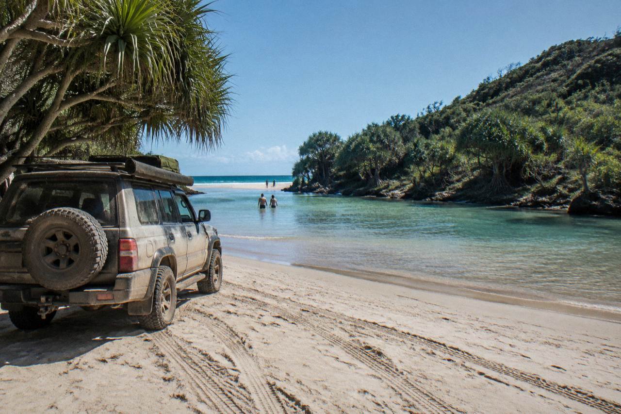 Four wheel drive tour vehicle parked on a wide sandy beach beside clear blue water