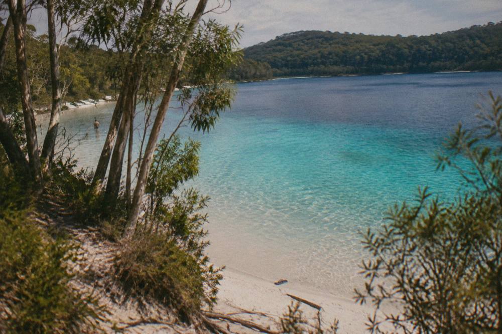 Clear turquoise water over white sand at a freshwater lake rimmed by forest