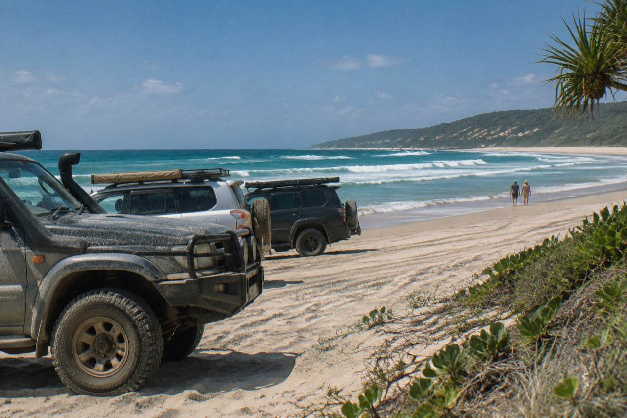 Four wheel drive vehicles parked on a wide sandy beach beside turquoise ocean at K'gari