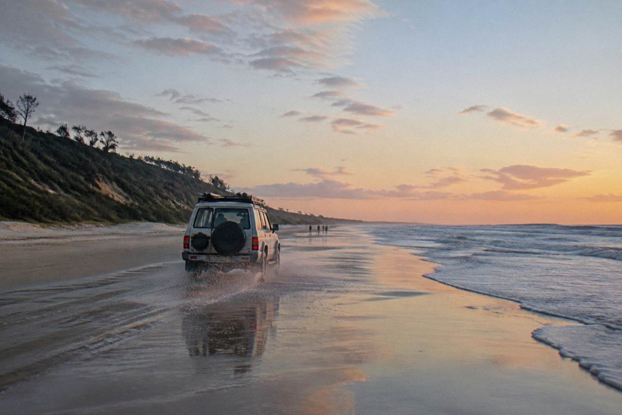 A four wheel drive vehicle travelling along a wide sandy beach beside the ocean