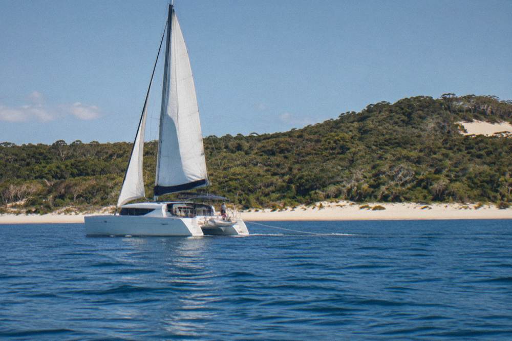 Catamaran on calm blue water near a sandy island shoreline