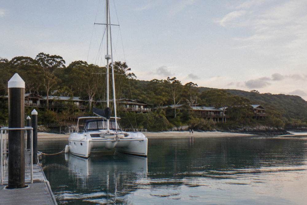 A catamaran boat moored near a sandy island shoreline under a wide sky