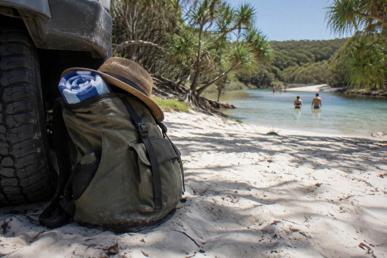 A packed day bag resting on the sand beside a four wheel drive vehicle on a beach