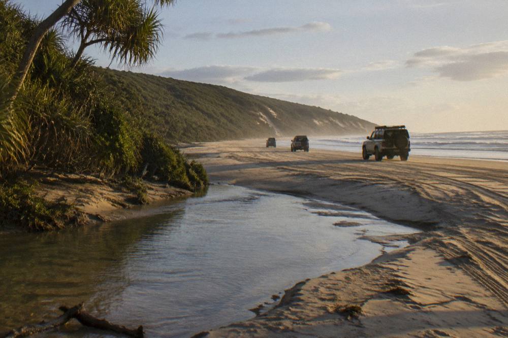 Four wheel drive vehicles travelling along a wide sandy beach at low tide
