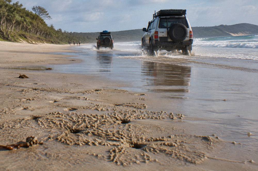 Four wheel drive vehicles travelling along a firm wet sand beach at low tide