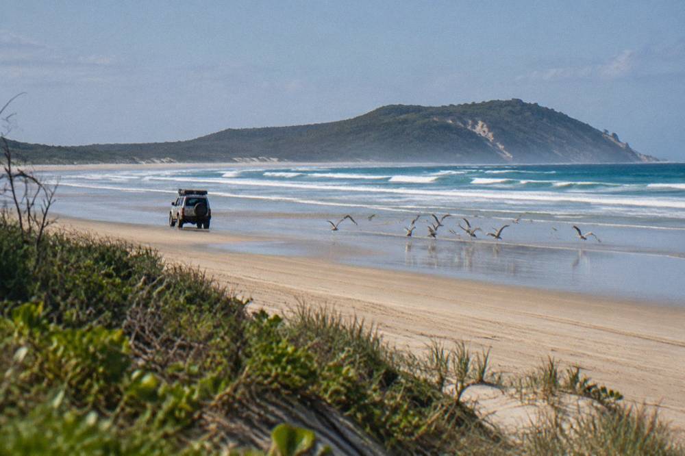 A four wheel drive vehicle travelling along a wide sand beach at low tide