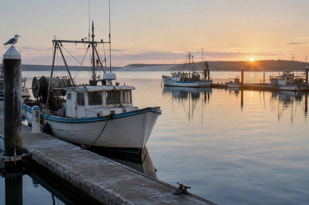 A small coastal town waterfront at sunrise with calm water and moored boats