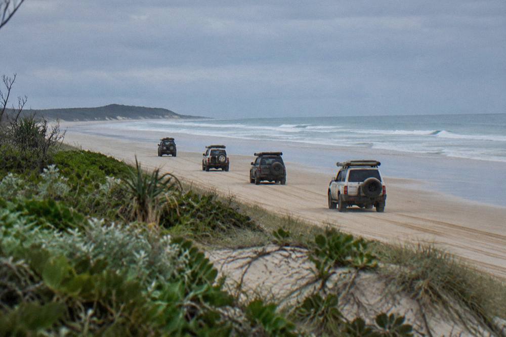 A group of four wheel drives travelling along a firm sand beach at low tide