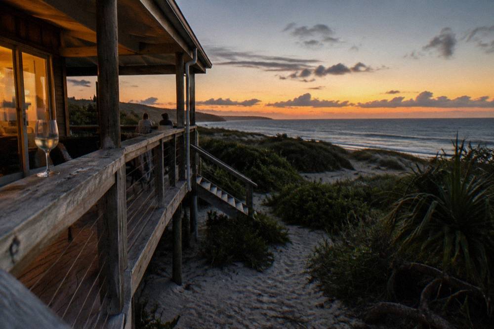 A timber beach house verandah overlooking sand dunes and the ocean at dusk