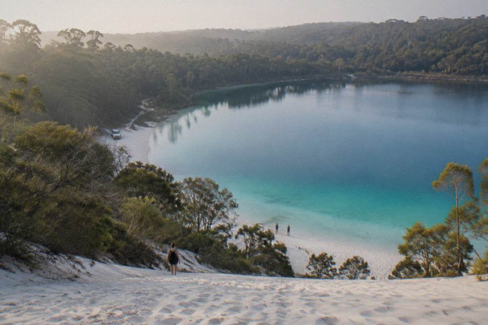 A clear freshwater lake ringed by white sand and tall eucalypt forest