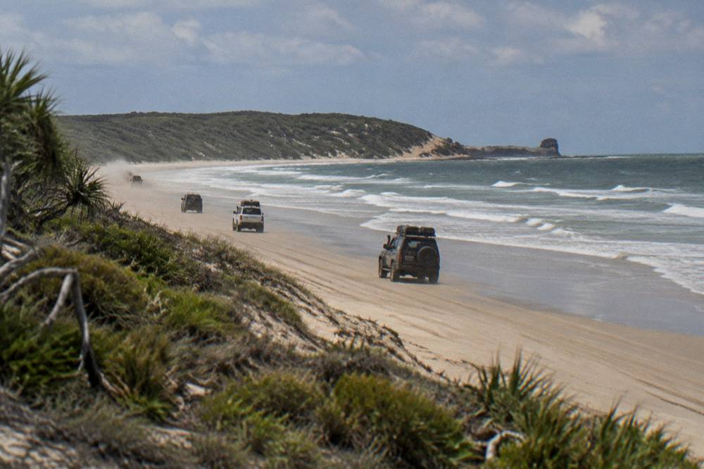A convoy of four wheel drive vehicles travelling in a line along a sandy beach