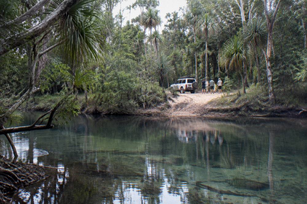 A small group of visitors standing beside a parked four wheel drive vehicle on a sandy track