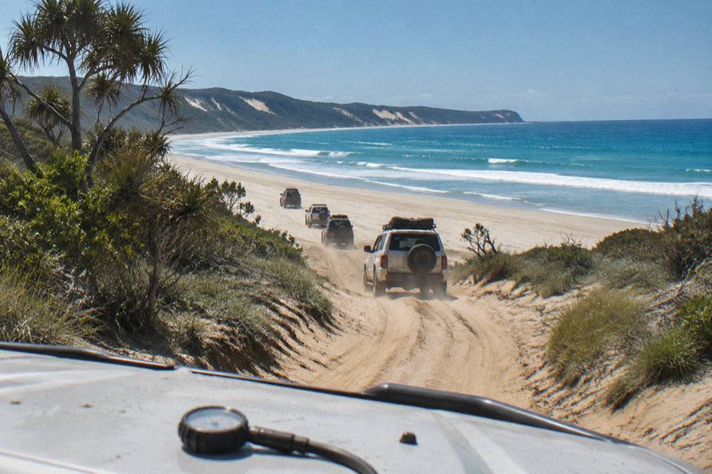 A convoy of four wheel drive vehicles following a lead vehicle along a sand track