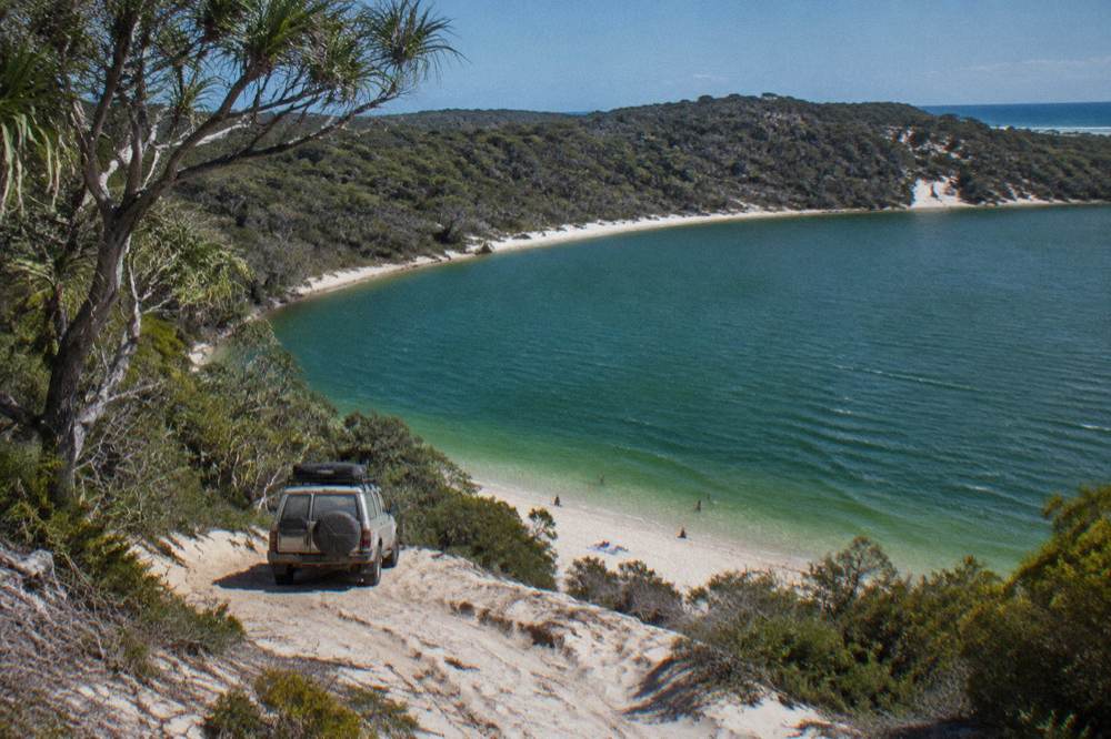 A tour vehicle parked beside a freshwater lake ringed by pale sand