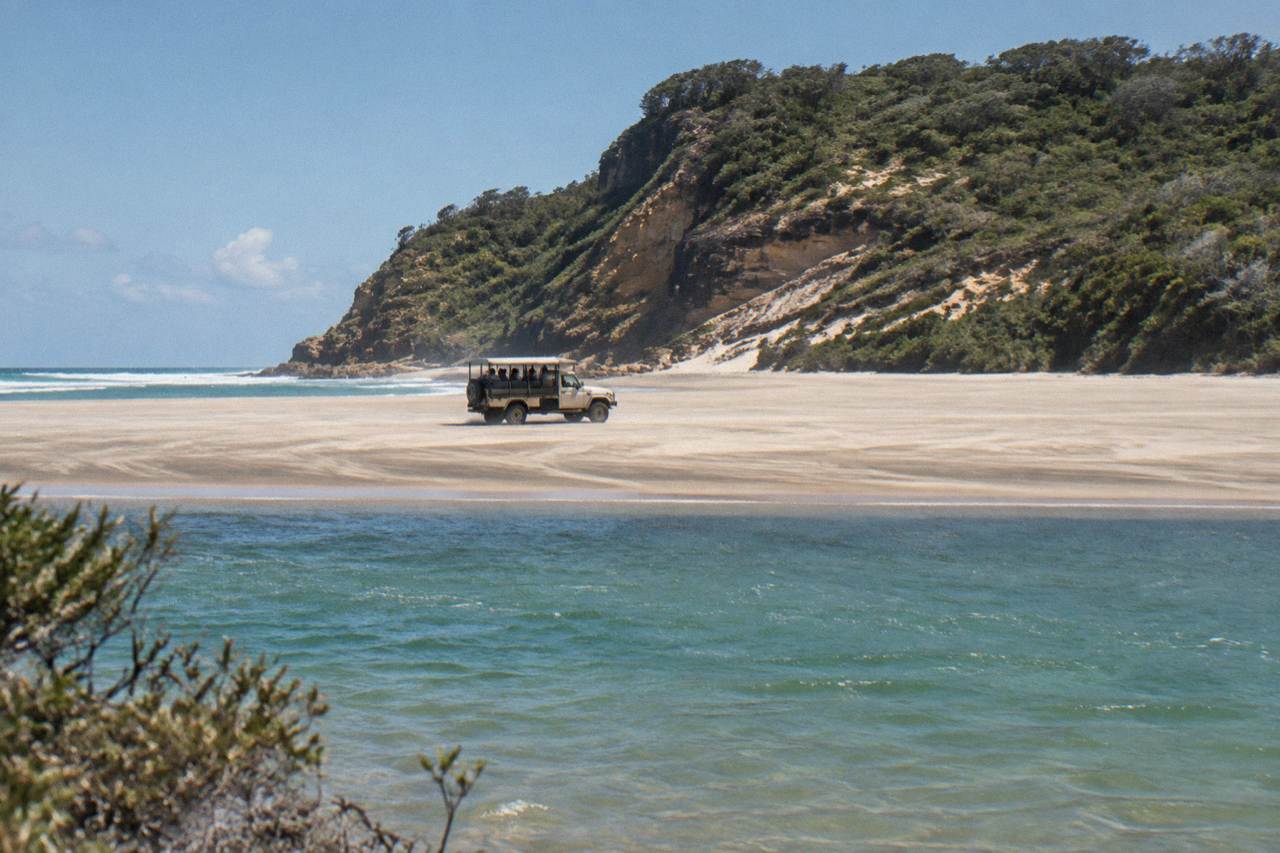 A four wheel drive vehicle on a wide sandy beach beside clear water