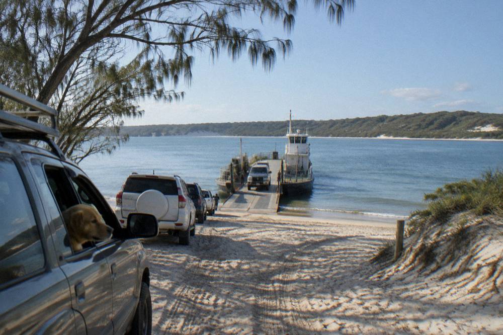 A vehicle barge loading at a mainland sand spit ramp in morning light