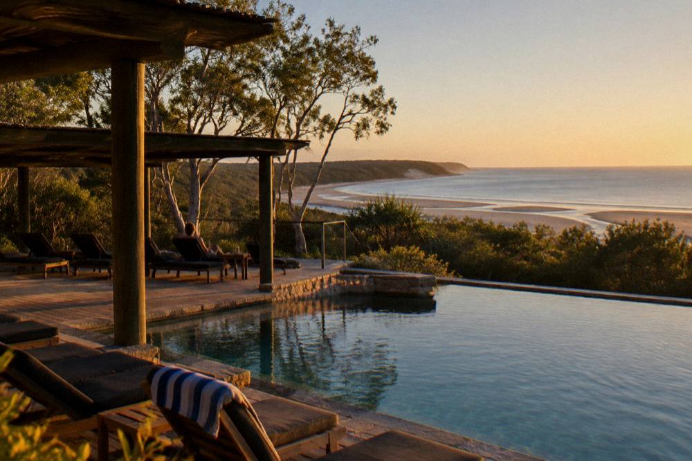 A resort deck and pool area overlooking a wide sandy beach in late afternoon light