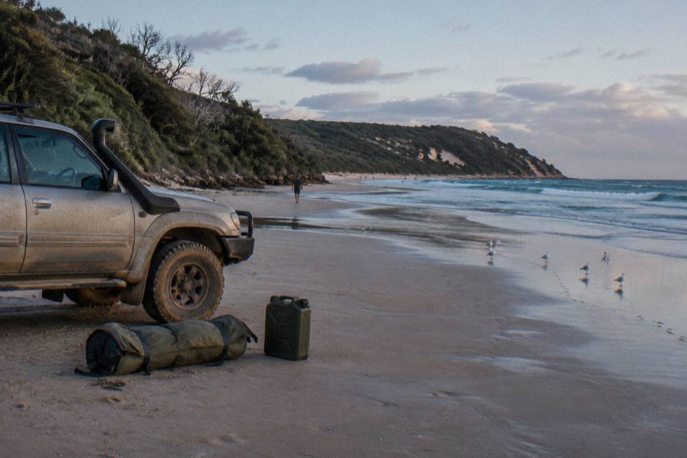 Four wheel drive vehicle parked on a firm sand beach beside camping gear at low tide