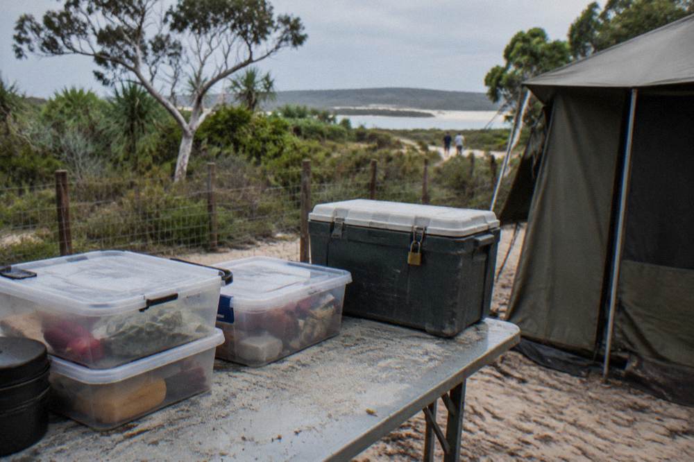 Sealed food storage containers and a locked cool box on a camp table beside a tent