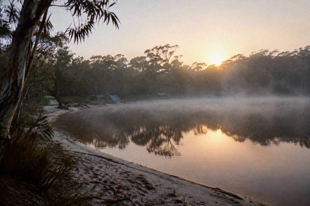 Campsite at sunrise with mist over a freshwater lake surrounded by sand and forest