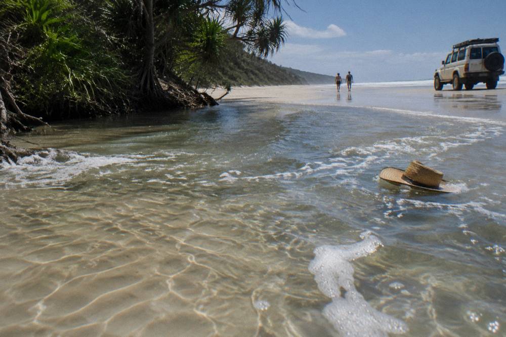 A four wheel drive tour vehicle parked on hard wet sand beside a shallow creek flowing to the sea