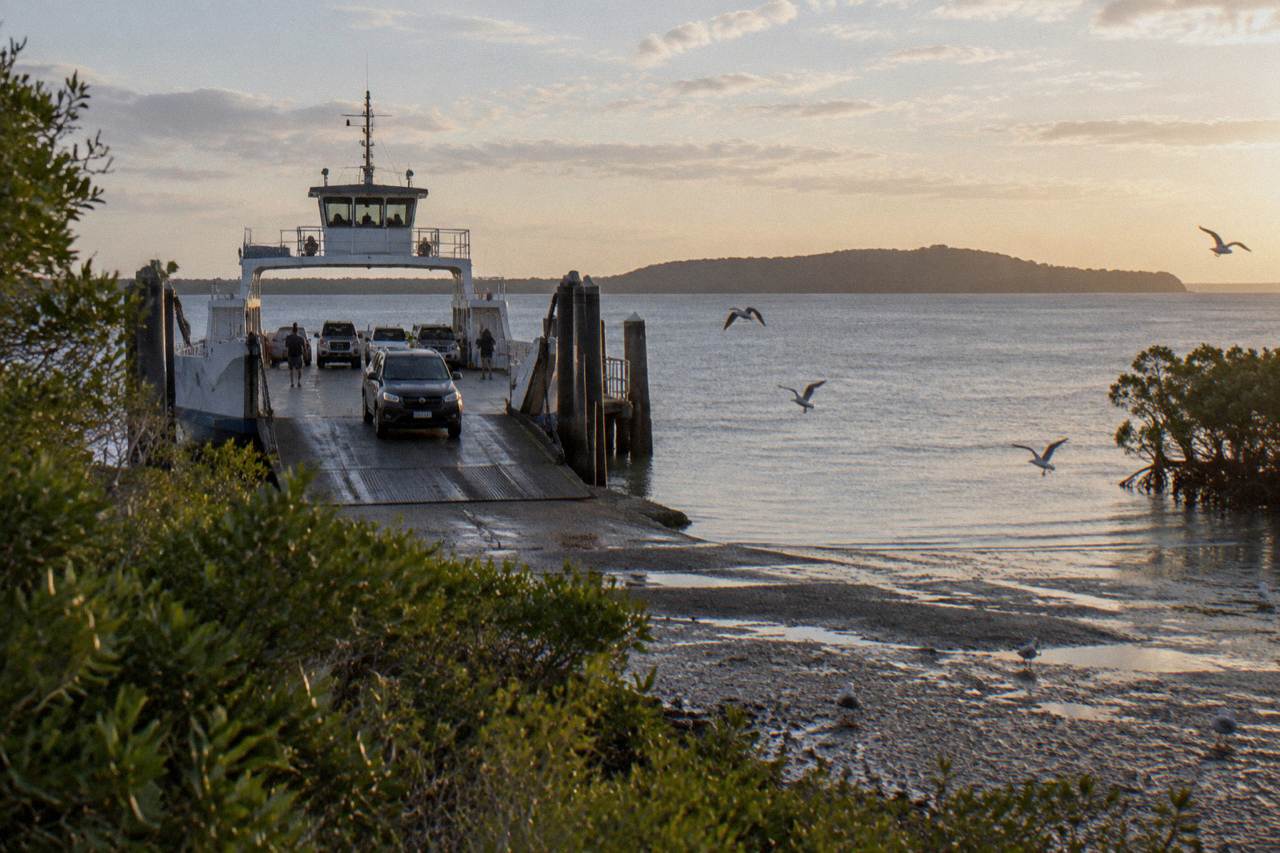 A vehicle barge loading at a sheltered bay crossing towards a sand island on the horizon