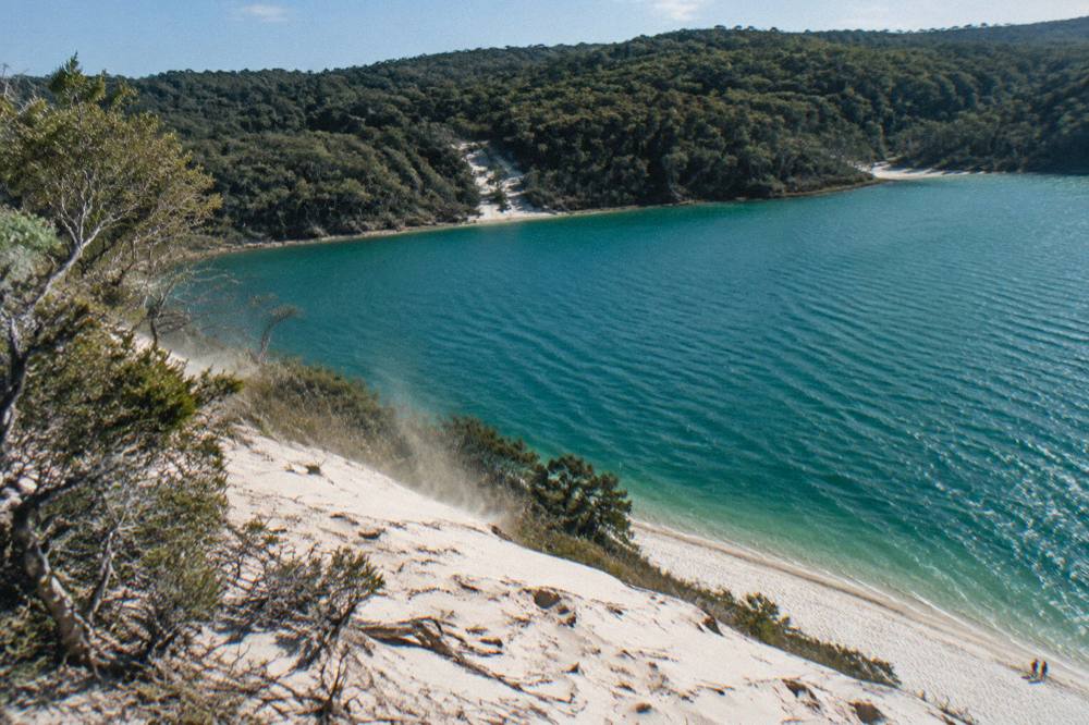 Calm turquoise freshwater lake ringed by white sand and forest under a clear sky
