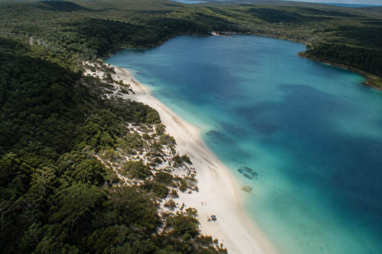 Aerial view of a long sand island with turquoise lake water set among green forest