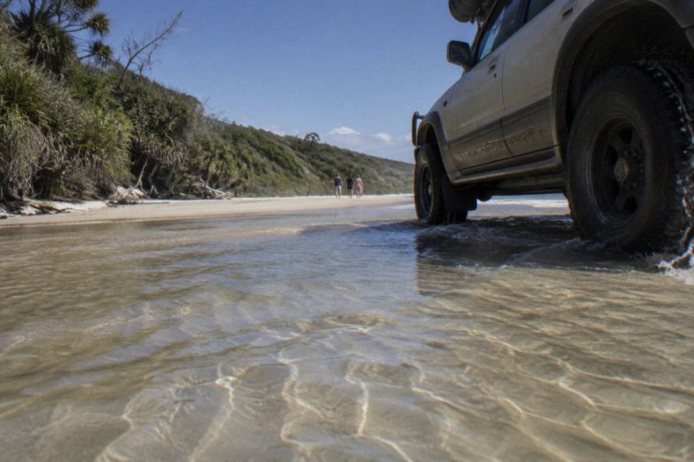 A four wheel drive vehicle driving on firm wet sand near the waterline of a wide beach