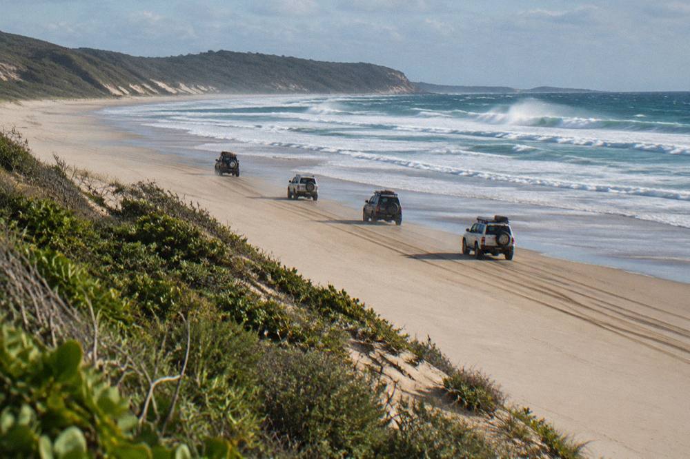 A convoy of four wheel drive vehicles travelling in a line along a sand beach