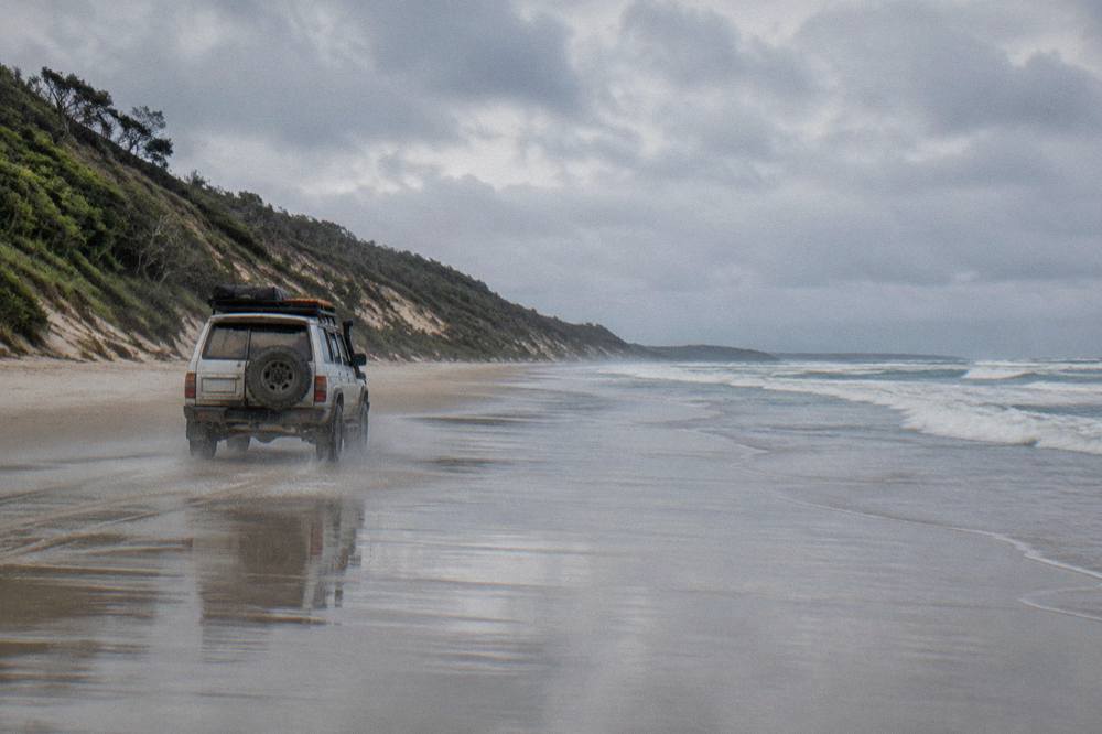 A four wheel drive tour vehicle driving along a firm wet sand beach at low tide