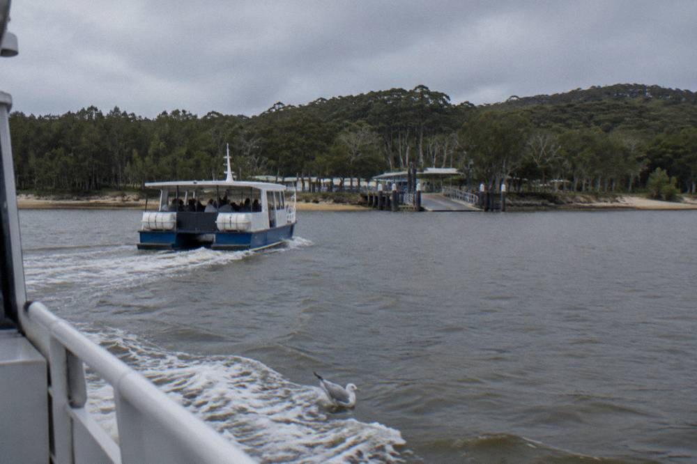 A small passenger ferry crossing calm open water toward a forested island shoreline