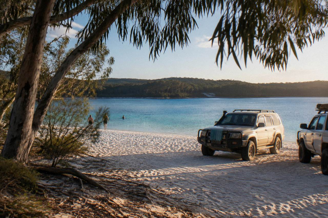 Four wheel drive vehicles parked on a wide sandy beach beside turquoise lake water