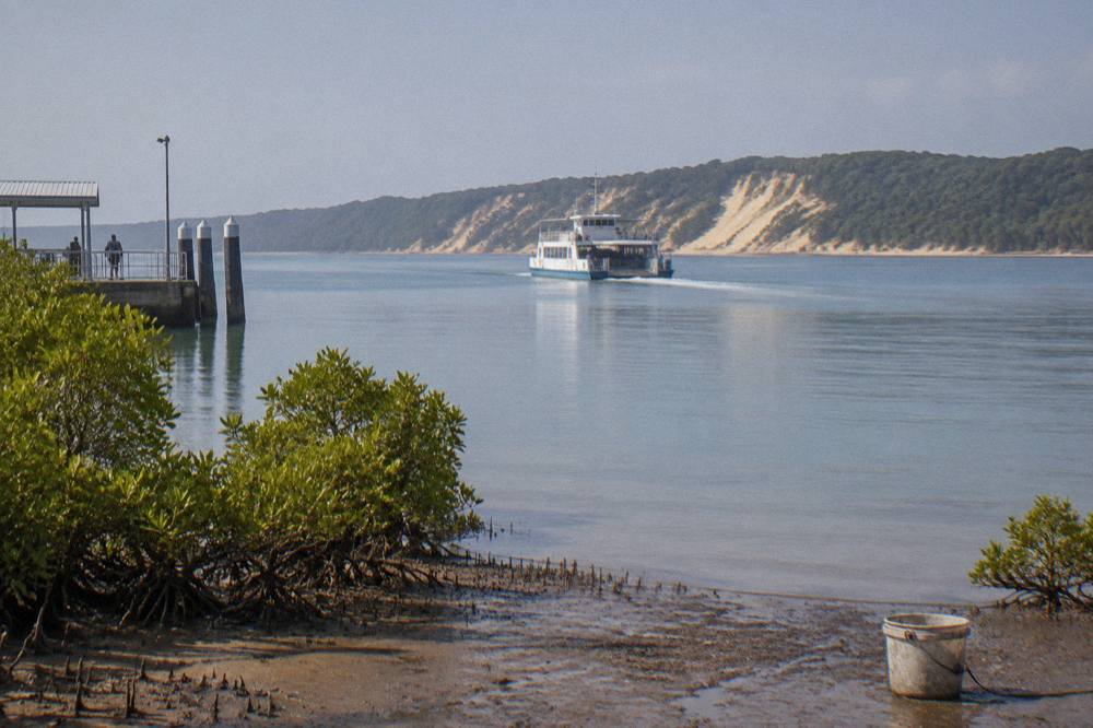 A passenger ferry travelling across calm blue water toward a forested sand island