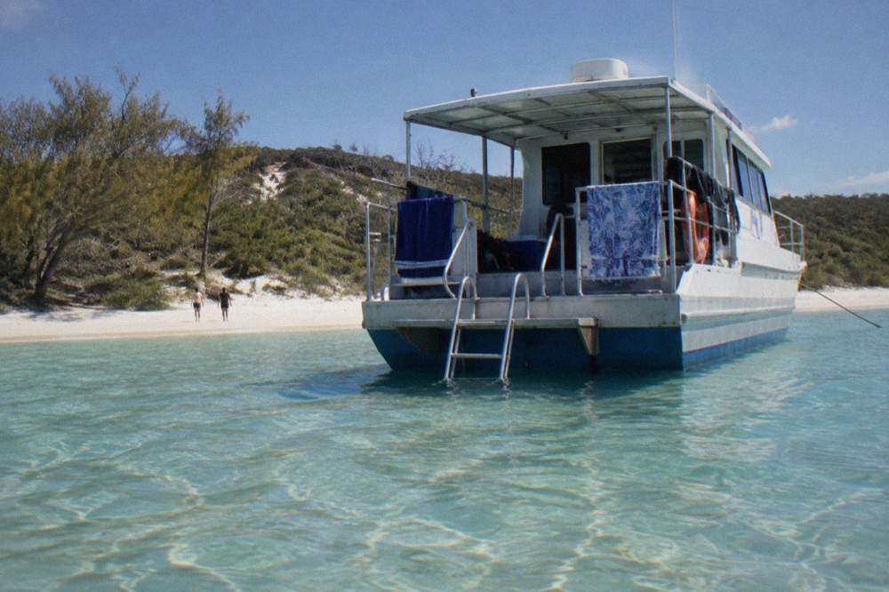 A small expedition boat anchored beside a remote sandy beach with clear shallow water
