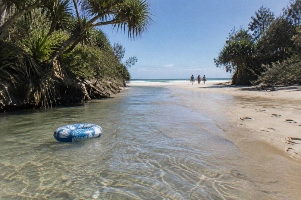 A clear shallow creek flowing over pale sand into the ocean on a wide beach
