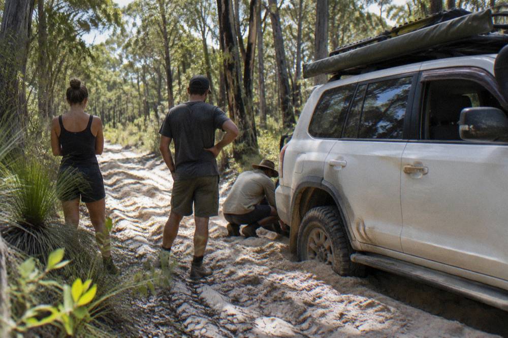 A small group of travellers standing beside a four wheel drive vehicle on a sandy track