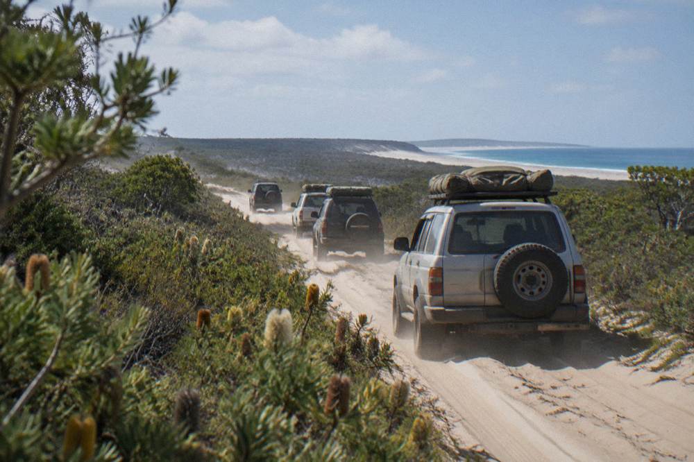 A line of four wheel drive vehicles travelling in convoy along a sandy island track