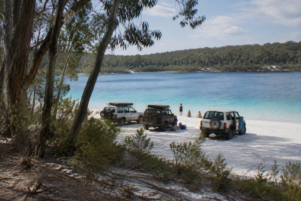 A small group of four-wheel-drive vehicles parked together at a freshwater lake on a sand island