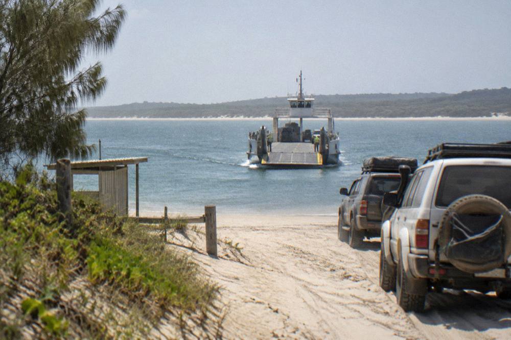 A vehicle ferry approaching a sandy landing point on an island shoreline