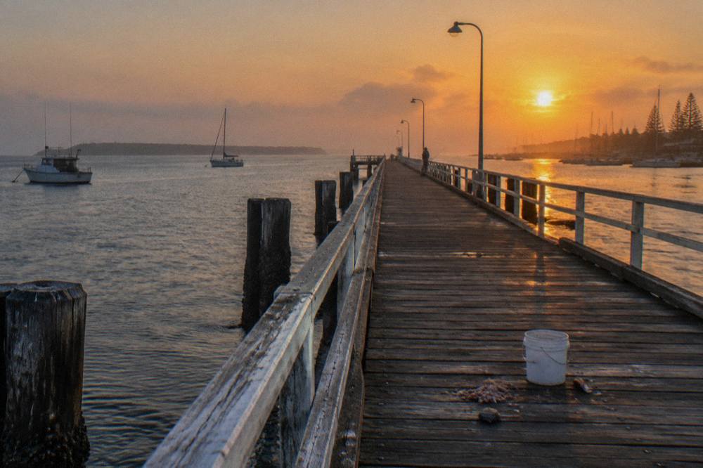 Long timber pier extending over calm shallow bay water at sunrise
